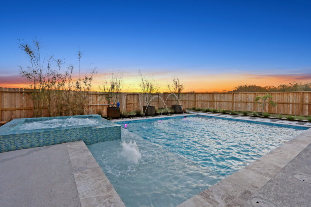 IMG_9949 - Sage Pools, Scapes & Design Backyard pool at sunset with a raised spa, bubbling water, tiled edges, and a wooden privacy fence in the background.