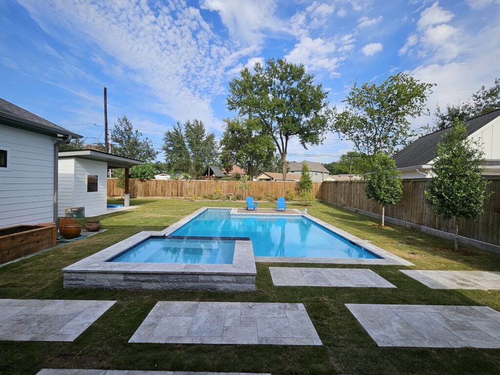 20261019_161713 - Sage Pools, Scapes & Design Backyard scene with a rectangular pool, stone deck, and two blue lounge chairs by a wooden fence.
