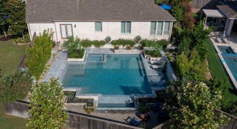 IMG_1275 - Sage Pools, Scapes & Design Aerial view of a backyard with a rectangular in-ground pool, spa, and stone deck adjacent to a white, single-story house.